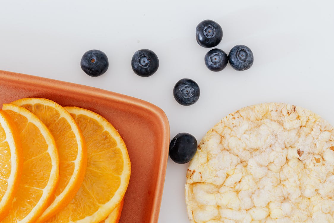 Free From above of fresh orange slices placed on cutting board near blueberries and rice cracker on white surface Stock Photo
