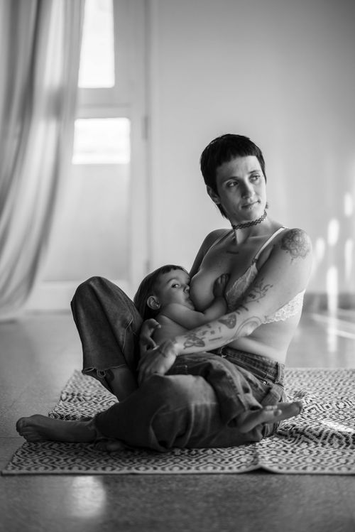 Free A black and white image of a tattooed mother breastfeeding her child indoors, capturing intimate and nurturing moments. Stock Photo