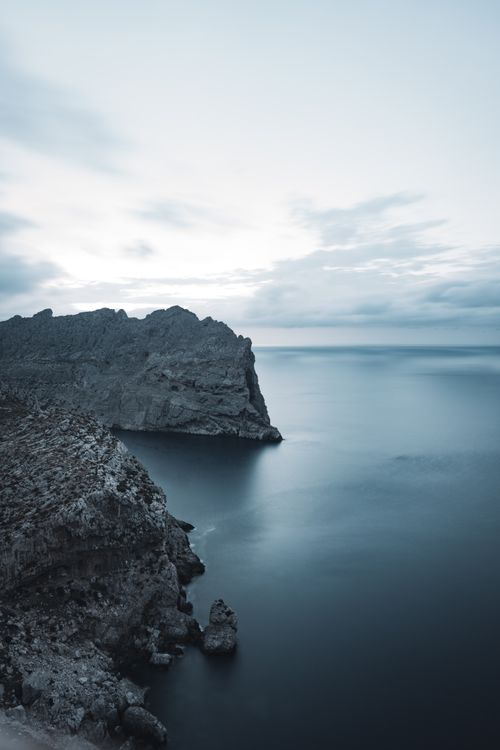 Free Scenic view of a rocky coastline in Spain at dusk, with tranquil sea and cloudy sky. Stock Photo