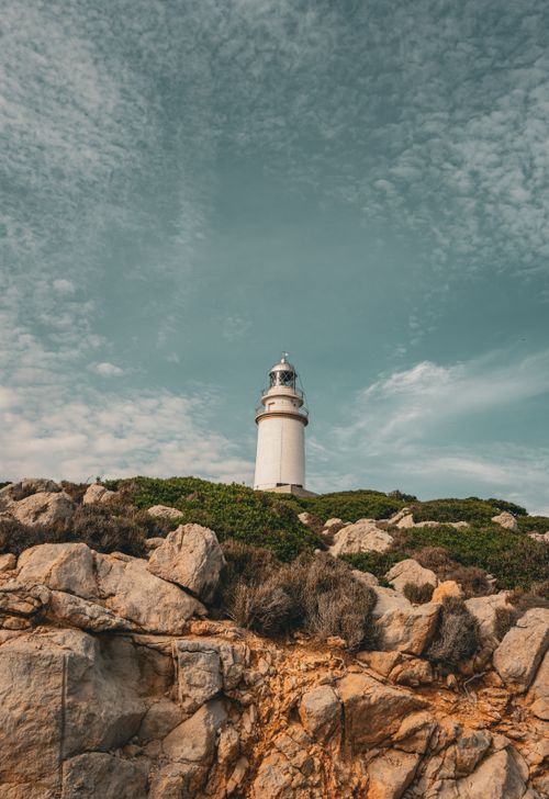 Free A peaceful lighthouse stands on a rocky shoreline under a partly cloudy sky in Ibiza, Spain. Stock Photo