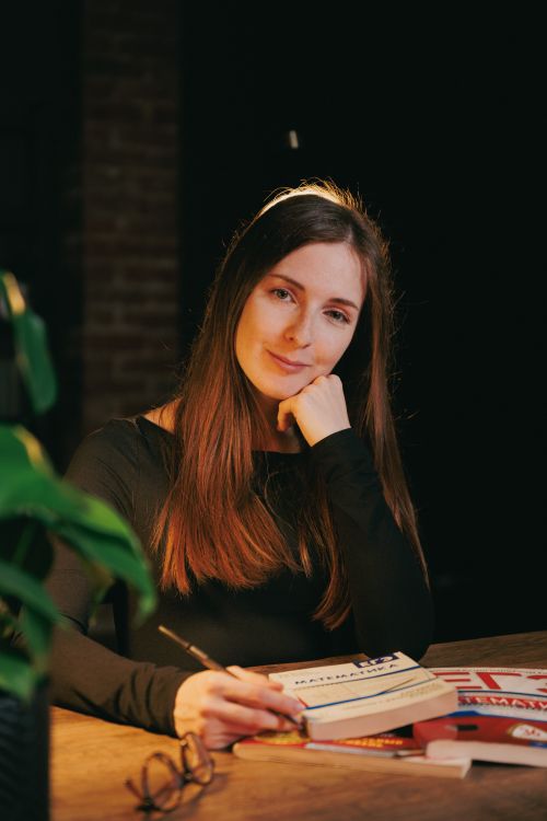 Free Portrait of a young woman sitting at a desk with books, studying in ambient lighting. Stock Photo