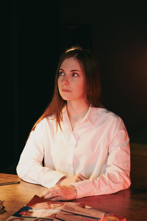 Free A thoughtful woman in a white shirt sits at a table with soft lighting creating a moody atmosphere. Stock Photo