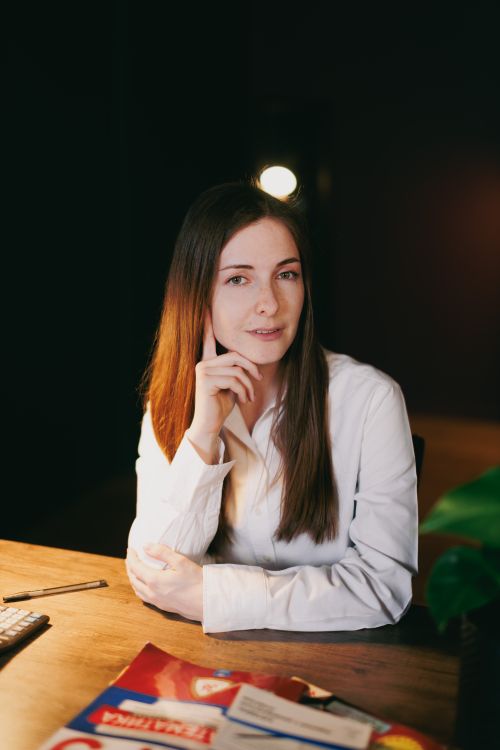 Free A confident woman in business attire sits at a desk in a warmly lit office setting. Stock Photo