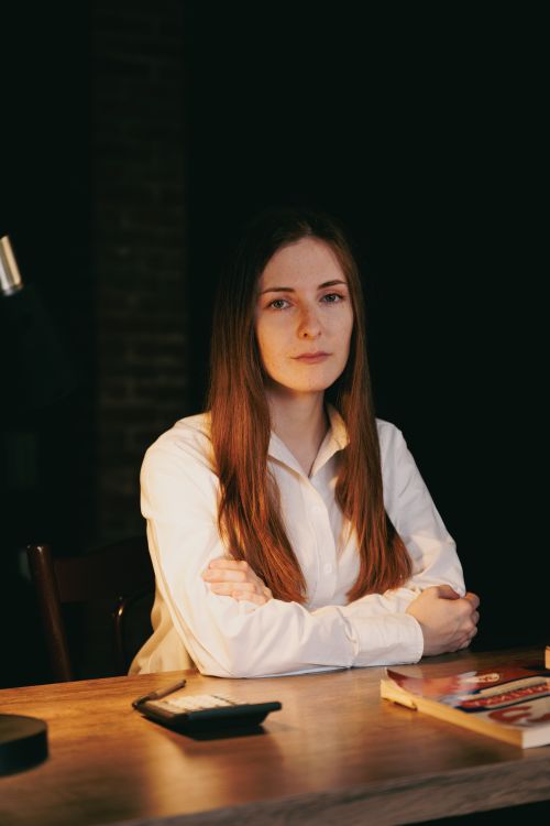 Free Young woman sitting at a desk in dim lighting, exuding confidence. Ideal for work and business themes. Stock Photo