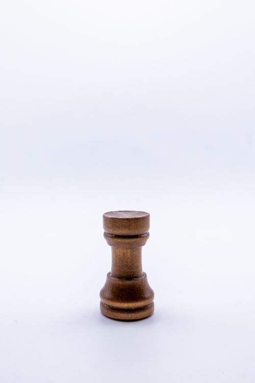 Free A single wooden rook chess piece stands on a plain white background, highlighting simplicity. Stock Photo