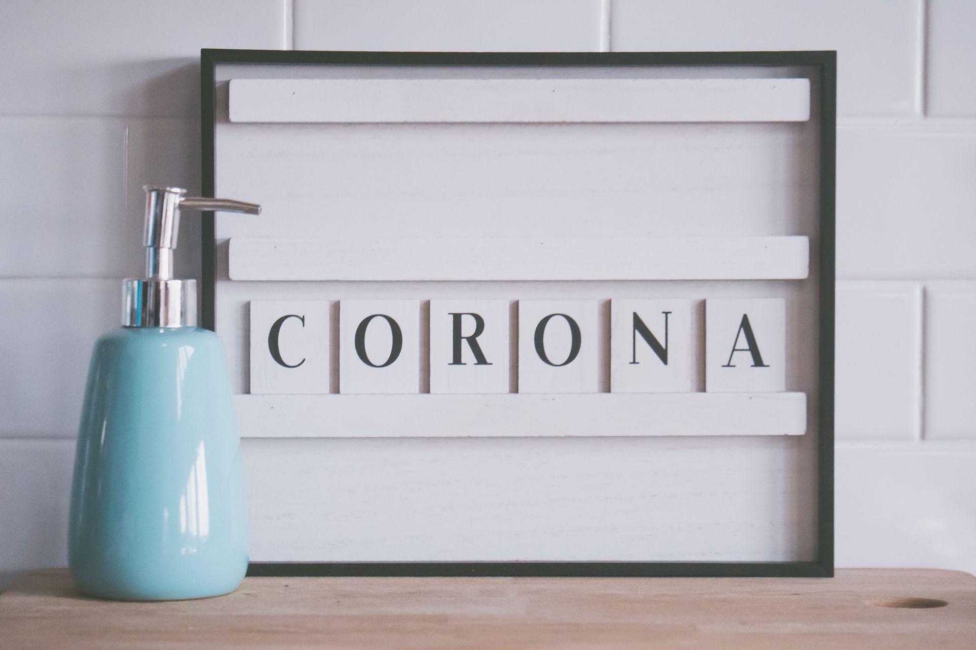 Blue dispenser with liquid soap placed near board with word CORONA in bathroom