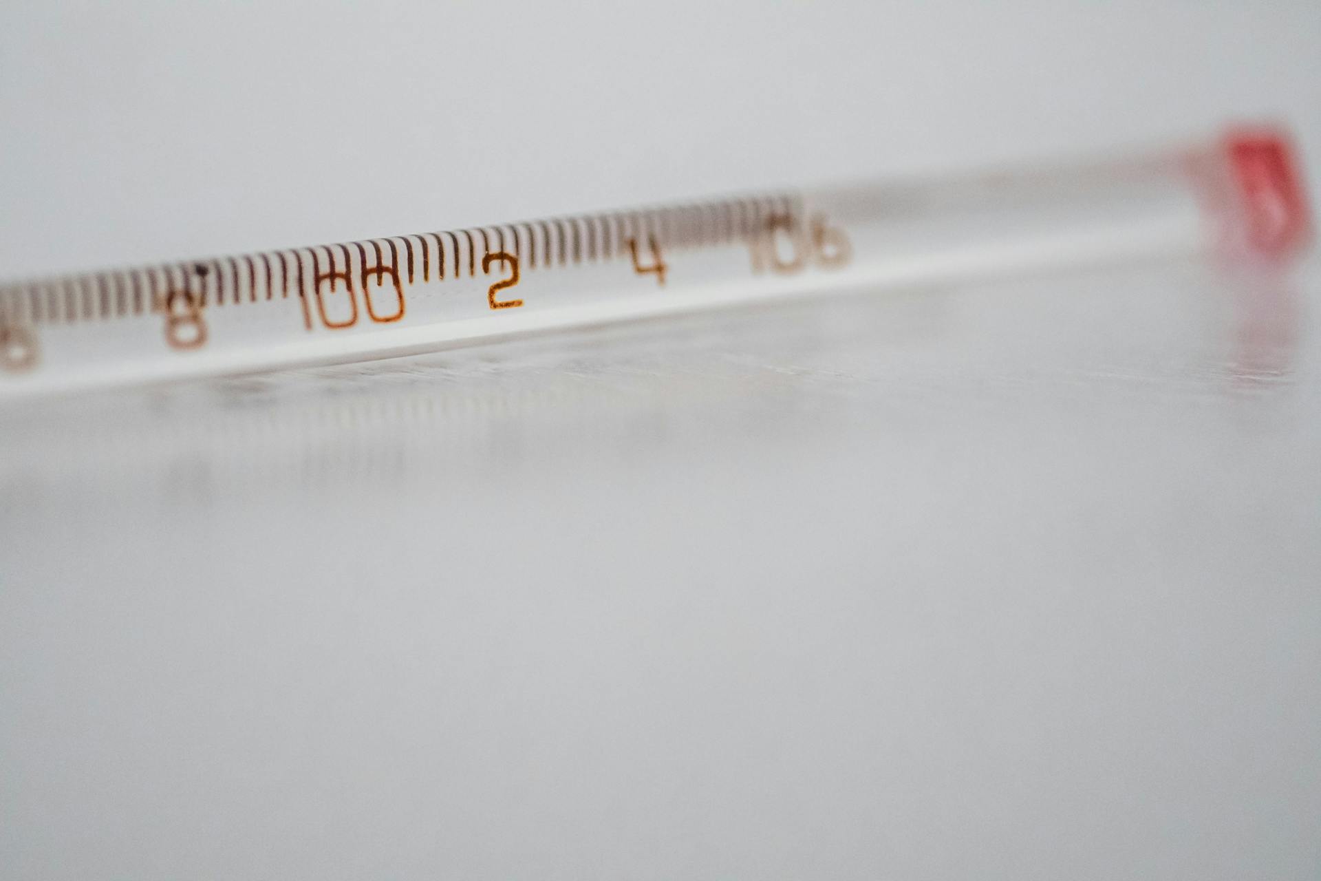 Detailed close-up of a mercury glass thermometer on a white surface, showing temperature measurements.