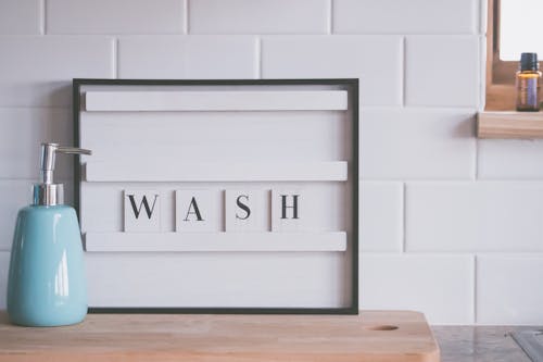 Board with word WASH placed near soap dispenser on counter in light bathroom representing concept of hygiene and coronavirus prevention