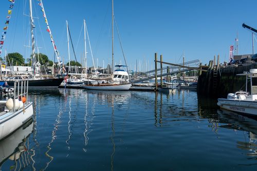 Free A serene marina with various yachts docked under a clear blue sky, reflecting on calm waters. Stock Photo
