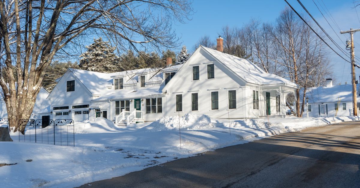 A serene winter scene of a snow-covered house and road under a clear blue sky.
