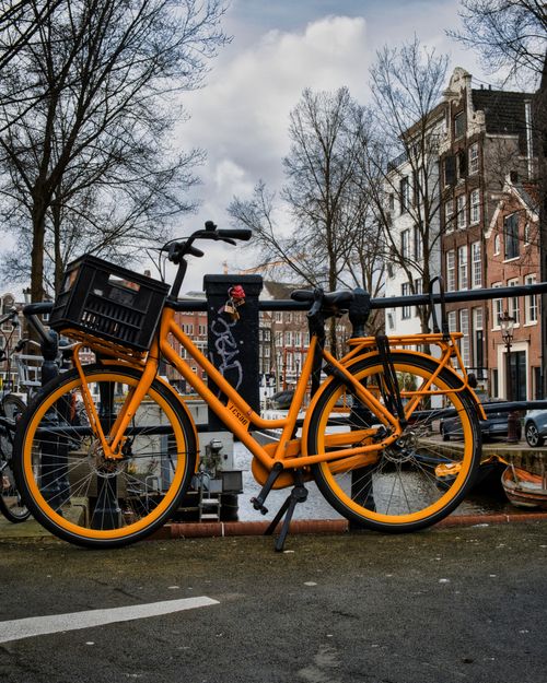 Free Bright orange bicycle parked on a canal bridge in Amsterdam, showcasing urban life and iconic architecture. Stock Photo
