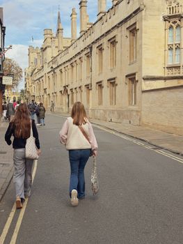 A typical day in Oxford with people walking by historic university buildings under a blue sky.