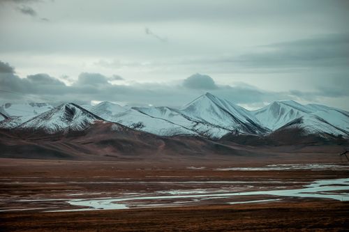 Free A breathtaking view of snow-covered mountains under cloudy skies with vast plains. Stock Photo