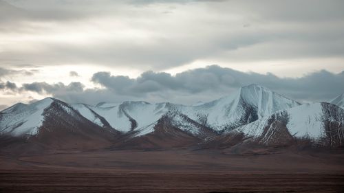 Free Serene snow-covered mountains under a dramatic cloudy sky, capturing a tranquil natural landscape. Stock Photo