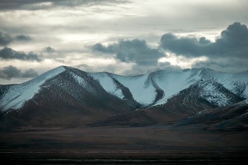 Free Breathtaking view of a snow-covered mountain range beneath a dramatic, cloudy sky. Stock Photo