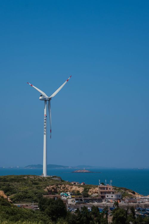 Free A lone wind turbine stands on a coastal hill with clear skies and the ocean beyond. Stock Photo