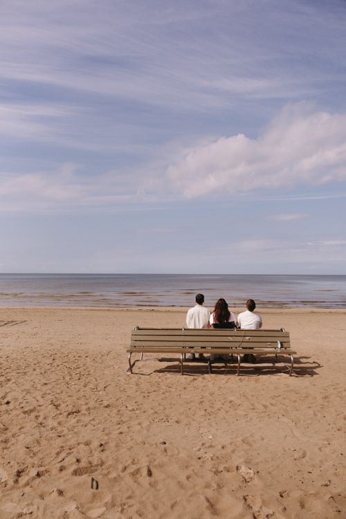 Free Three individuals sitting on a beach bench, gazing at the sea under a cloudy sky. Stock Photo