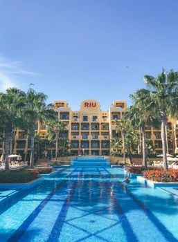 Stunning view of the pool area at Riu Hotel in Cabo San Lucas, featuring palm trees and bright architecture.