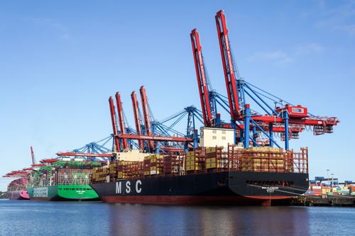 Free Dynamic view of container ships docked at Hamburg's bustling port terminal under clear blue skies. Stock Photo