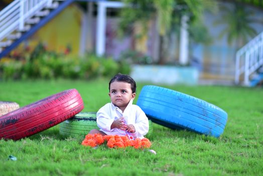 Cute baby playing on the grass with colorful tires as background in a creative outdoor setup.
