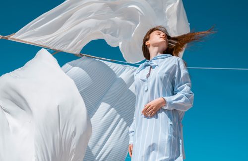 Free A woman in a white dress enjoying the breeze with clear blue sky and flowing sheets. Stock Photo