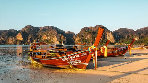 Free Explore the vibrant longtail boats on a tranquil Thai beach during sunset, surrounded by stunning karst formations. Stock Photo