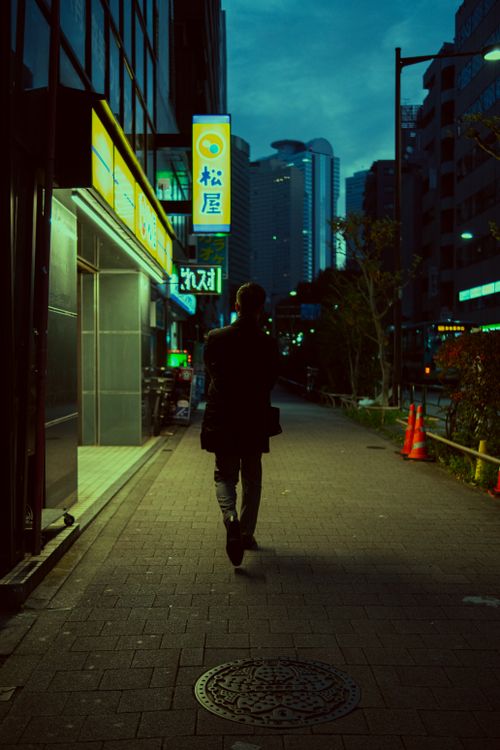 Free A person walks down a vibrant Tokyo street illuminated by bright signs at twilight. Stock Photo