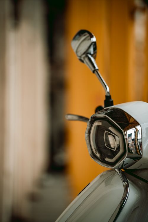 Free Close-up view of a classic Vespa scooter with a focus on its headlight and reflective mirror. Stock Photo