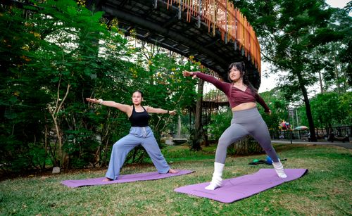 Free Two women practicing yoga poses on mats in an outdoor urban park in Jakarta. Stock Photo