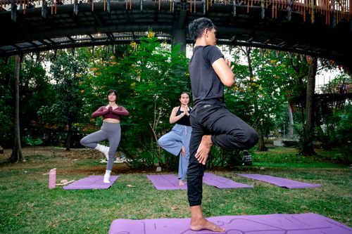 Free Men and women practicing yoga in a vibrant Jakarta urban park setting, focusing on wellness. Stock Photo