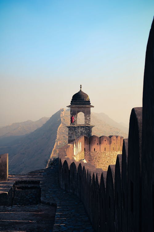 Scenery view of aged masonry wall with tower with cupola and spire on top near staircase behind mounts illuminated by artificial light in evening under serene sky