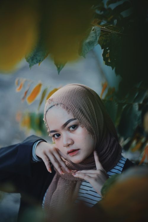Free A captivating portrait of a woman wearing a hijab, framed by lush green leaves. Stock Photo