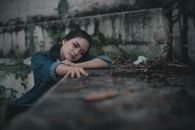 一名穿着牛仔裤夹克的悲伤沉思的少数族裔女青少年独自坐在公园旧石墙附近，看着镜头
