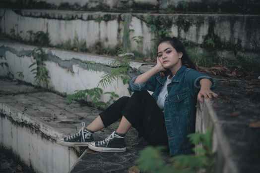 一位穿着休闲装的少女，坐在饱经风霜的户外台阶上，一脸沉思