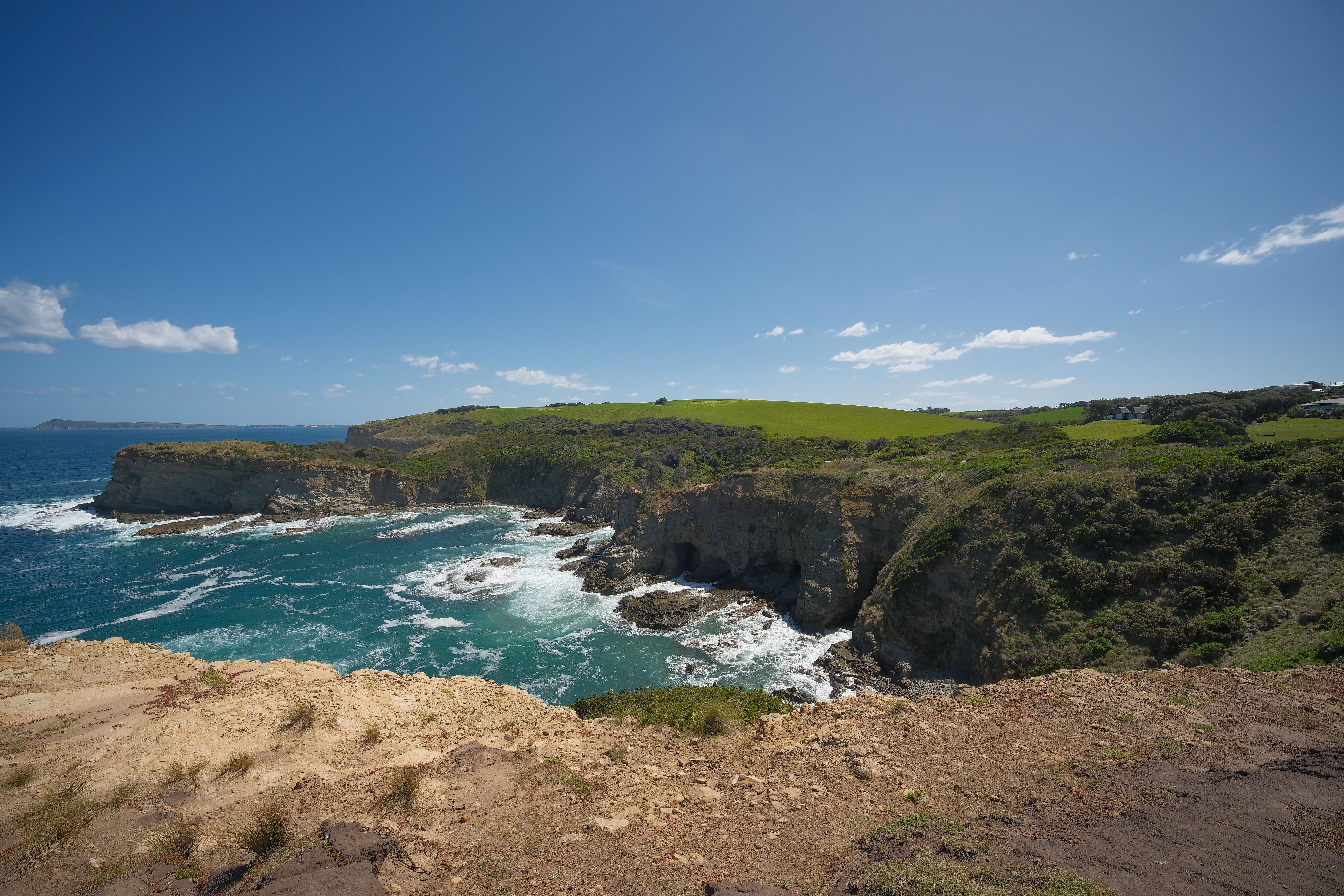 Expansive view of rugged coastal cliffs meeting the vibrant blue ocean under a clear sky.