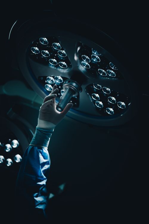Free A surgeon adjusts the overhead surgical light in a dimly lit operating room, creating a focused atmosphere. Stock Photo