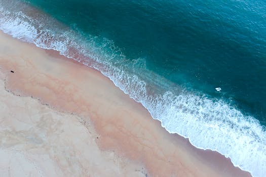 A stunning aerial shot showcasing a pristine beach with waves crashing on the sandy shore.