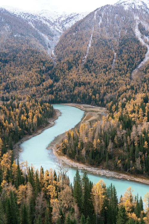 Free Tranquil autumn view of a river winding through a mountainous forest landscape, featuring vibrant fall colors. Stock Photo