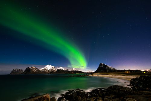 Free Aurora Borealis illuminates the night sky over snow-capped mountains and rocky coastline in the Arctic region. Stock Photo