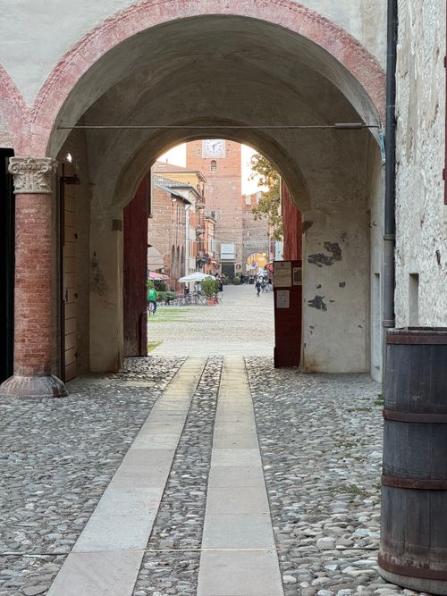 Free Cobblestone path through historic archway in Spilamberto, Italy, leading to town square. Stock Photo