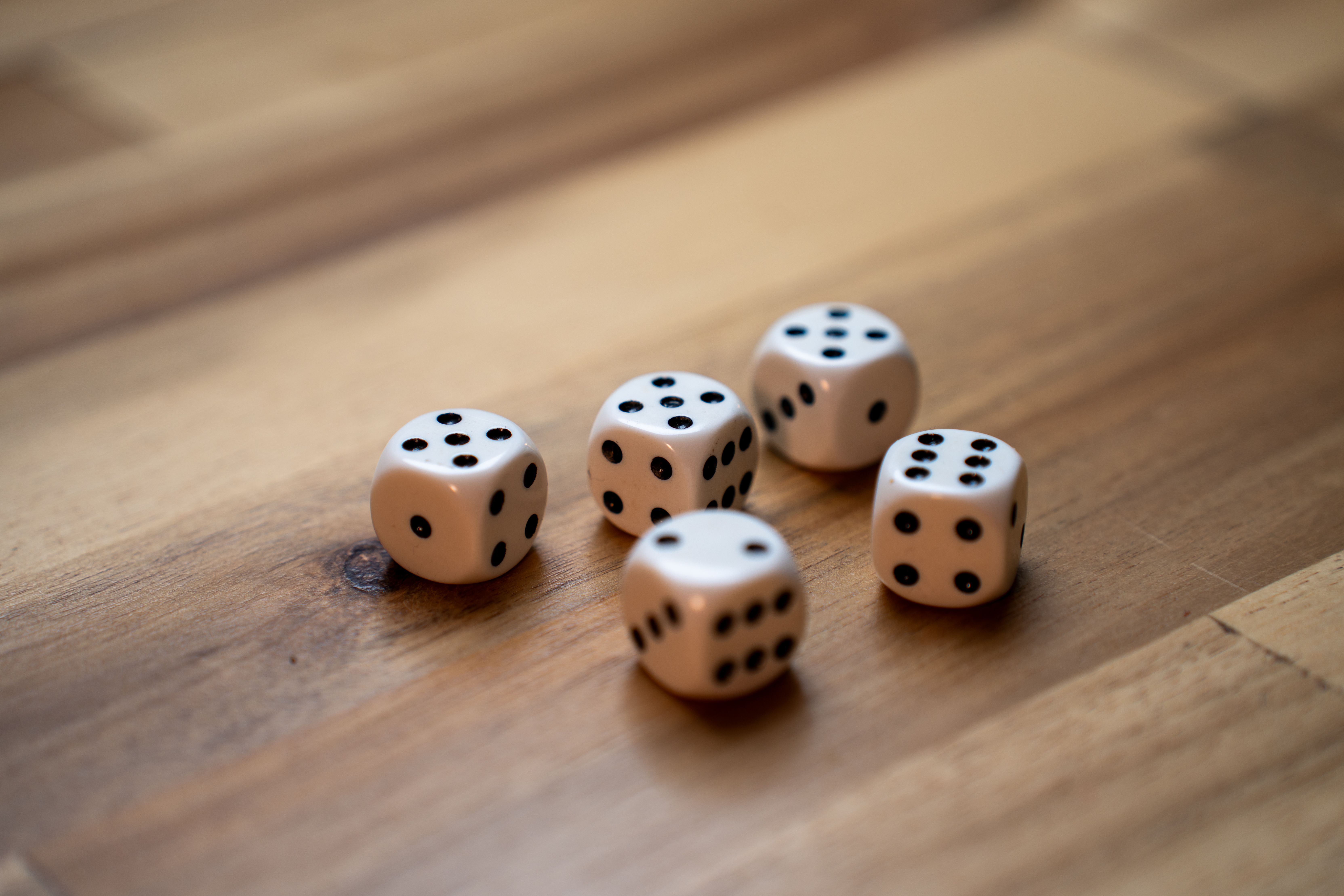 Close-up of five white dice with black dots on a wooden surface.