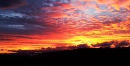 日落充满活力，令人叹为观止，与戏剧性的云和山形成剪影