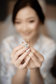 A bride delicately holds wedding rings, showcasing beautiful nail art.