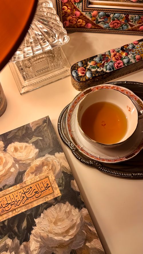 Free Tea cup on saucer with floral decor and Arabic calligraphy book in elegant setting. Stock Photo