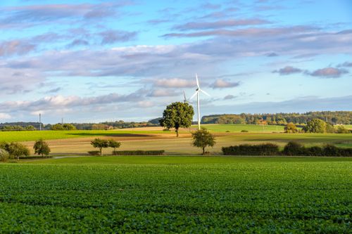 Free A beautiful rural landscape in Coesfeld, Germany featuring fields, trees, and a wind turbine under a clear sky. Stock Photo