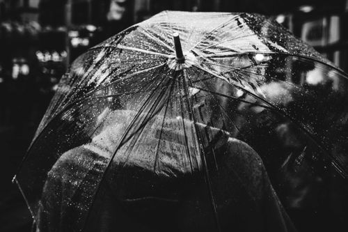 Free Captivating black and white photo of a person holding an umbrella during rain in an urban setting. Stock Photo