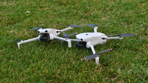 Free A pair of sleek white drones are positioned on a grassy lawn, ready for launch. Stock Photo