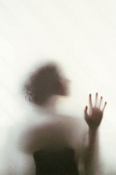 窗后站着一位触摸玻璃的性感梦幻匿名女性剪影