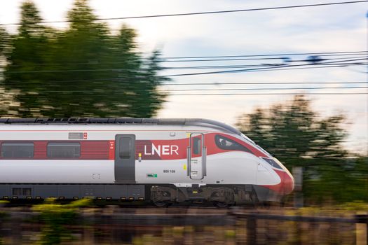 Side view of a high-speed LNER train moving swiftly outdoors, blurred background.