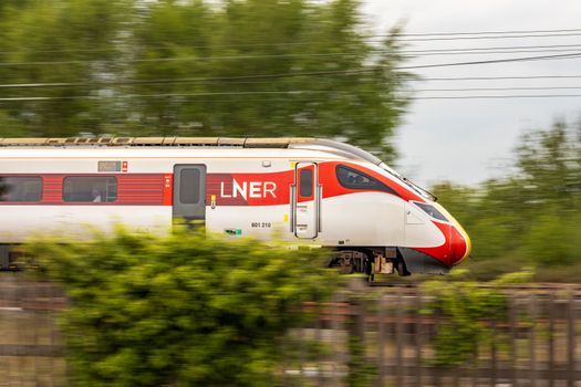 LNER train captured at high speed through lush countryside, showcasing modern rail travel.
